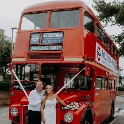 Ben and his newly-wedded wife standing in front of a red London double-decker bus, which has been hired out for a private wedding party.